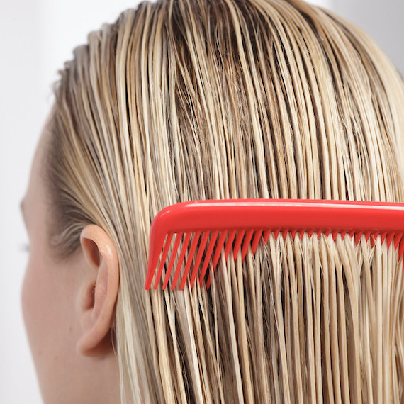 Model runs a red comb through their wet hair.