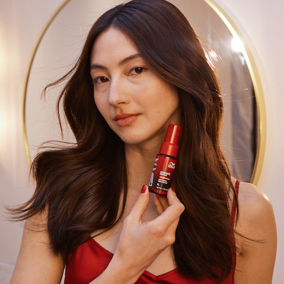 Model with long, loosely curled, dark brown hair holds up ULTIMATE REPAIR Night Serum.