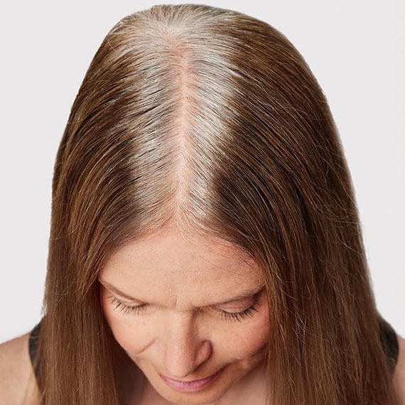 Close-up of model’s gray roots through light brown hair.