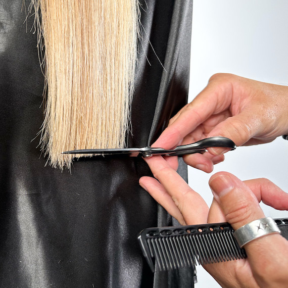 A close-up of a model’s straight, blonde hair being trimmed by a hairdresser.