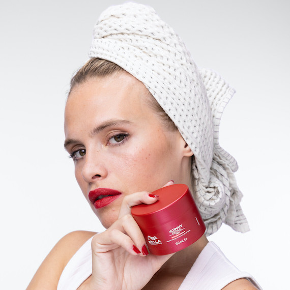 Model with damp hair wrapped in a towel holds up the ULTIMATE REPAIR Mask.