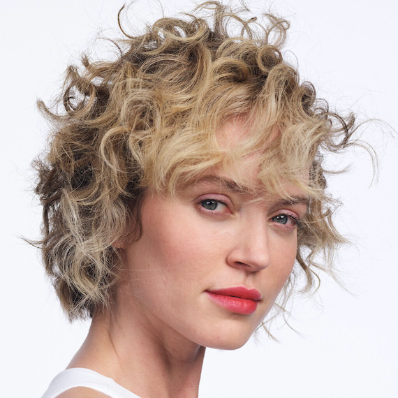Model with short, blonde, curly hair faces the camera. 