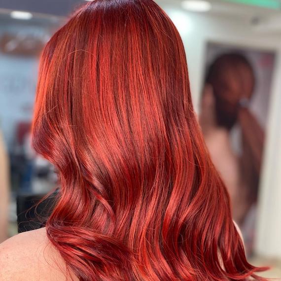 Back of woman’s head with long, loosely waved, bright red hair, created using Wella Professionals.