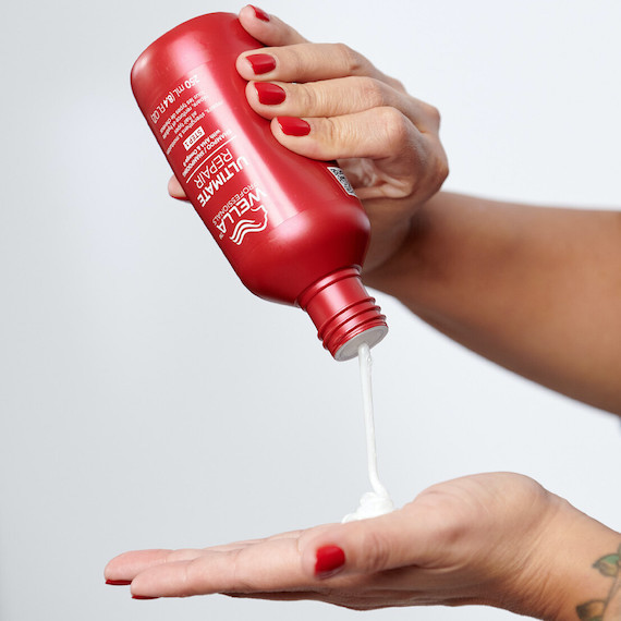 Eine Flasche Ultimate Repair Shampoo wird in eine Handfläche gedrückt. Die Nägel der Person sind rot lackiert