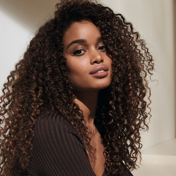 Model with long, dark curly hair smiles at the camera.