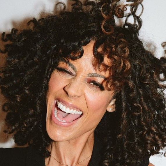 Model with dark brown, curly hair smiles at the camera. 