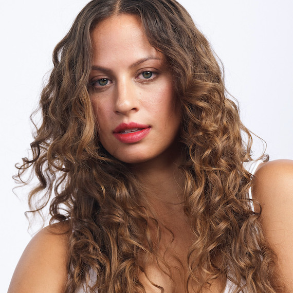 Model with long, curly, light brown hair looks directly into camera.