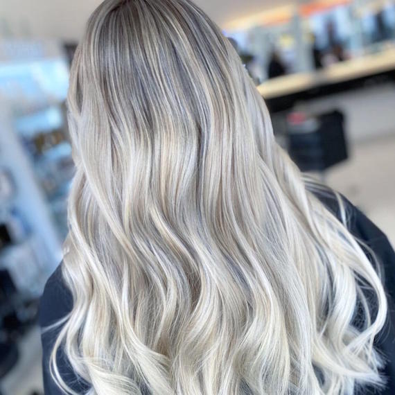 Back of woman’s head with long wavy platinum blonde hair and dark roots, created using Wella Professionals.