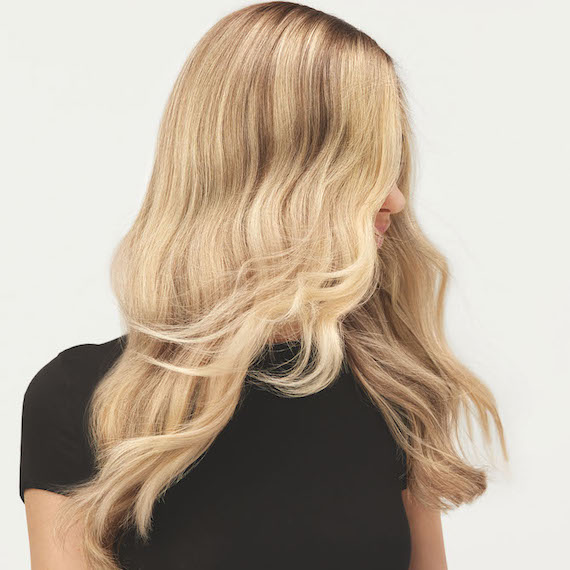 Model flicks her long blonde hair that’s been colored using the Illuminage technique by Wella Professionals. 