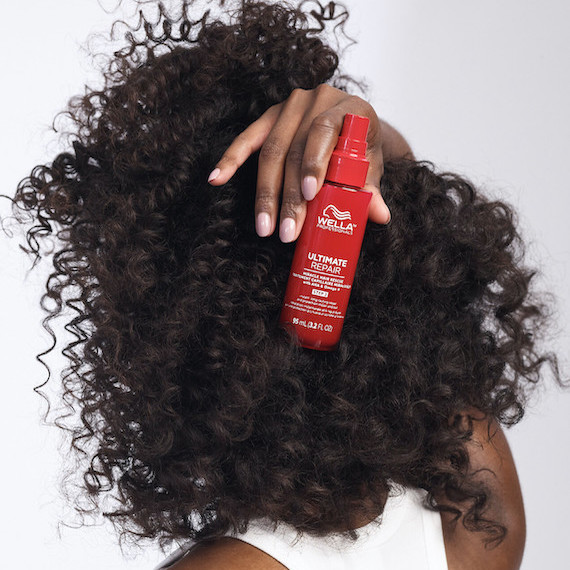 Model with dark, curly hair holds up ULTIMATE REPAIR Miracle Hair Rescue.