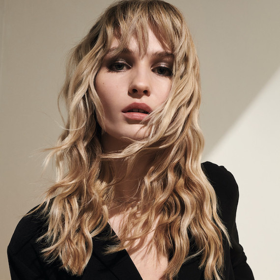 Model with long, wavy blonde hair coloured using Koleston Perfect by Wella Professionals looks at the camera 