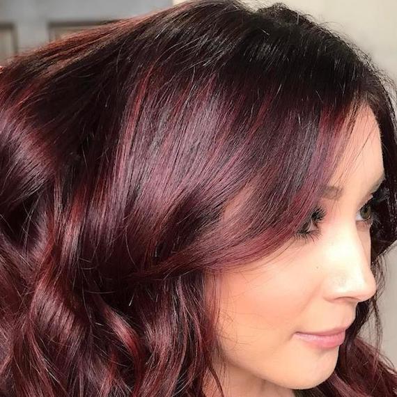 Woman with loosely curled, shiny, mahogany hair, created using Wella Professionals.