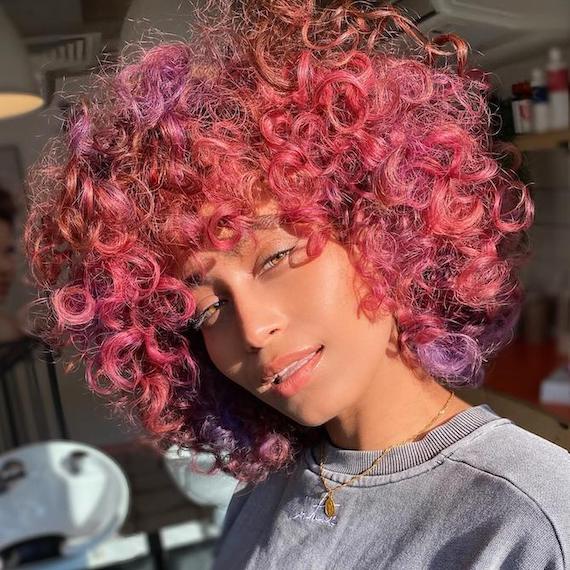Woman faces the camera with hot pink, curly hair, created using Wella Professionals.