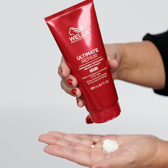 Model pours ULTIMATE REPAIR Conditioner from red bottle into palm of hand.