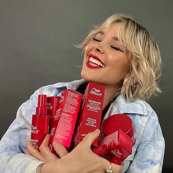 Model with short, blonde hair clutches a bundle of ULTIMATE REPAIR products.