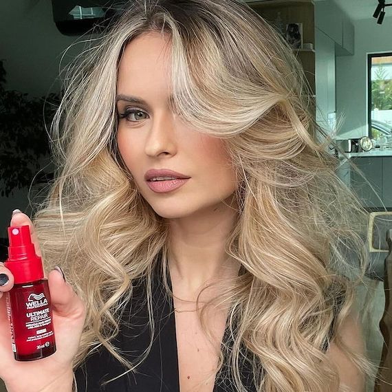 A model with long, loosely curled, blonde hair holds up a bottle of ULTIMATE REPAIR Miracle Hair Rescue.