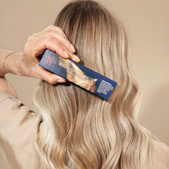 Model holds a box of Koleston Perfect Color in front of her long, wavy, vanilla blonde hair.