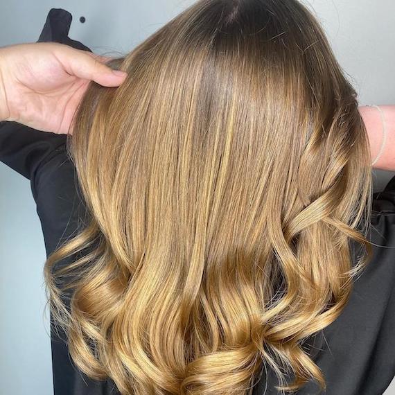 Back of woman’s head with long, loosely tonged, honey bronde hair, created using Wella Professionals. 