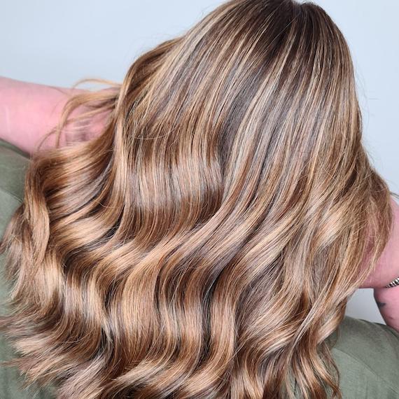 Back of woman’s head with wavy, mocha blonde, highlighted hair, created using Wella Professionals. 