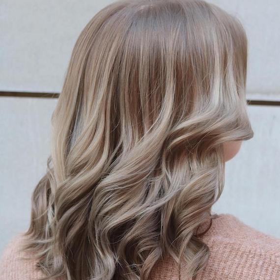 Back of woman’s head with shoulder-length, loosely curled hair and light mushroom blonde highlights, created using Wella Professionals.