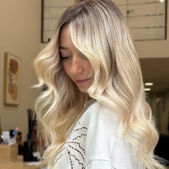 Model with loosely curled, vanilla blonde hair painted in micro-fine highlights.