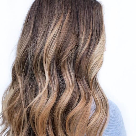 Back of woman's head with partial blonde balayage through long, wavy hair, created using Wella Professionals.