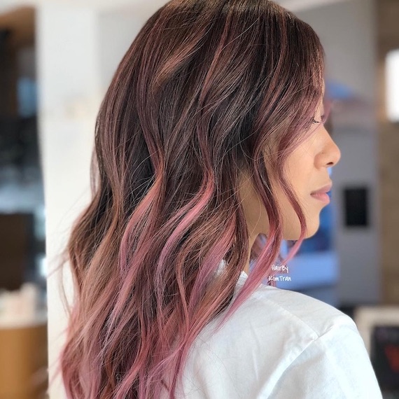 Side profile of model with dark brown hair and pastel pink balayage.