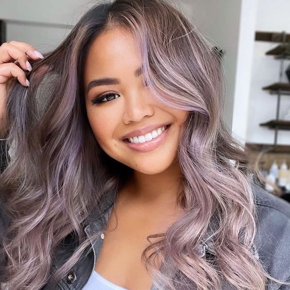 Model smiles at camera with long, gray blonde hair and pastel purple balayage.