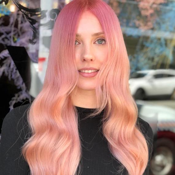 Model faces camera with long, wavy, pastel pink ombre hair.