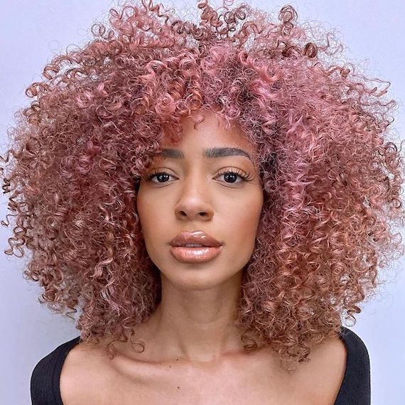 Model with full, voluminous, curly hair that’s a pastel rose gold colour.