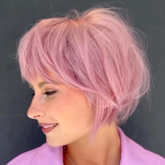 Model with short, tapered, bob haircut and bangs in a candy pink colour.