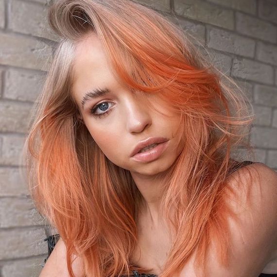 Model faces camera with a peach blonde balayage hair look.