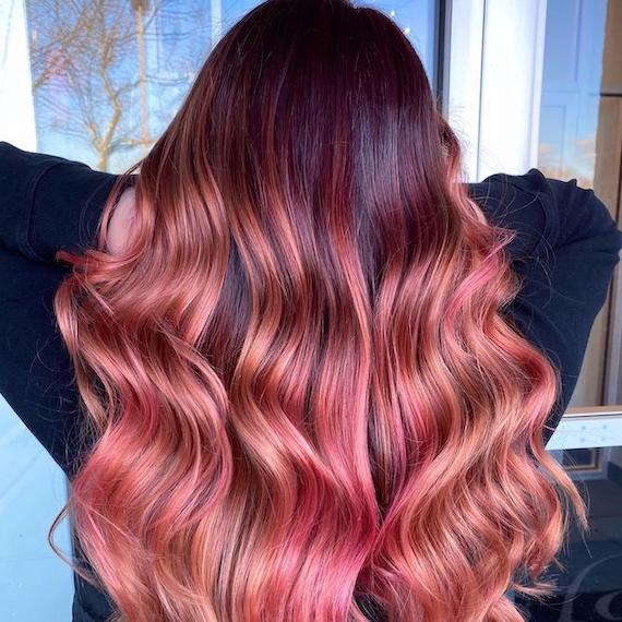 Back of woman’s head with long, brown, wavy hair and rose pink balayage.