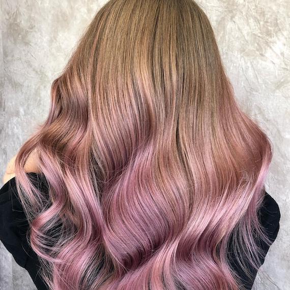Back of woman’s head with long, dark blonde hair and blush pink balayage.
