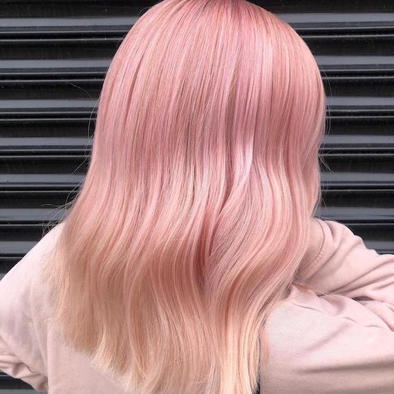 Back of woman’s head with pastel pink reverse balayage on platinum blonde hair.