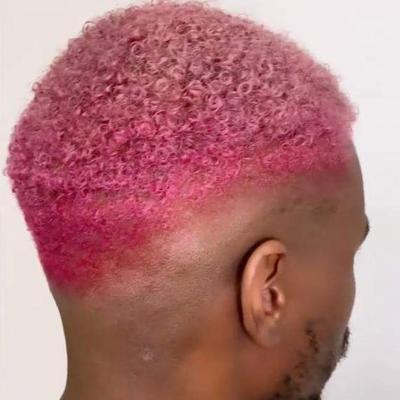 Back of model’s head showing short, curly, buzz cut hair with a pink ombre fade.