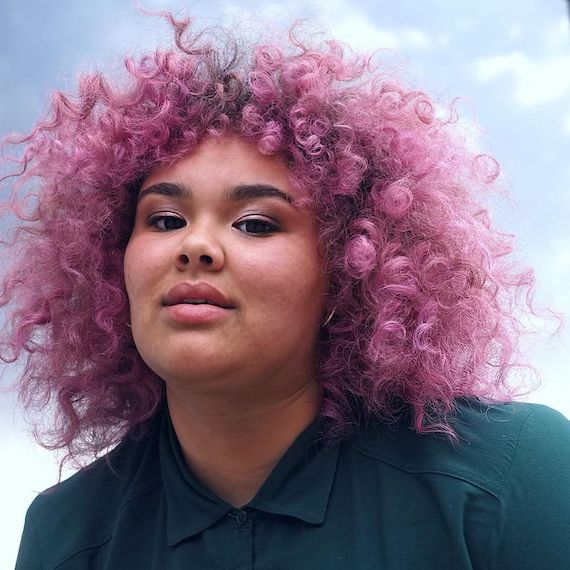 Model with curly hair, featuring deep rose roots and a pink ombre on the ends.