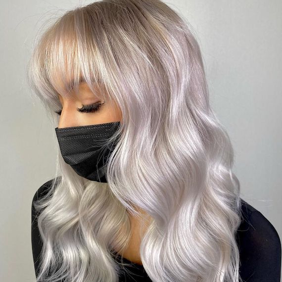 Side profile of model with platinum highlights through wavy blonde hair and bangs. 