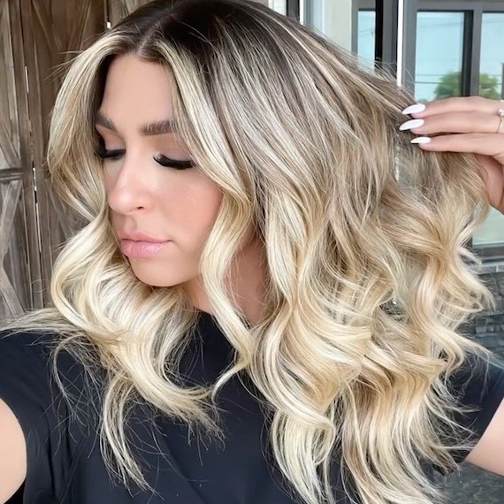 Model touches long, beachy, wavy hair, featuring platinum blonde ombre tones.