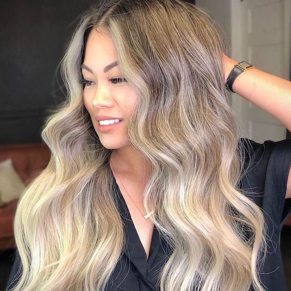 Model turns to the side, showing off super-long, wavy hair in an ash platinum ombre hue.