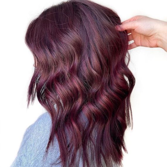 Side profile of model with wavy, burgundy plum brown hair