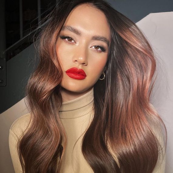 Model with subtle plum brown hair wears bright red lipstick and tilts her head at the camera