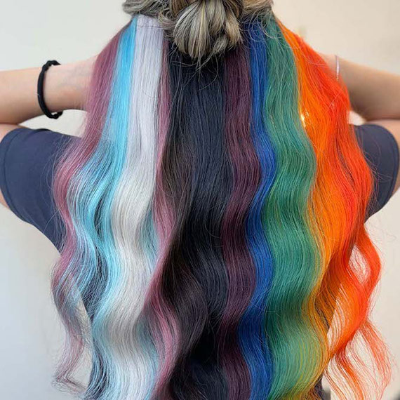 Model’s long, wavy hair is painted in colours from the Progress Pride flag, including pastel tones and bold brights.