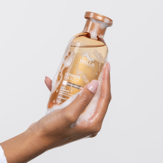 Model holding bottle of ULTIMATE SMOOTH Shampoo.