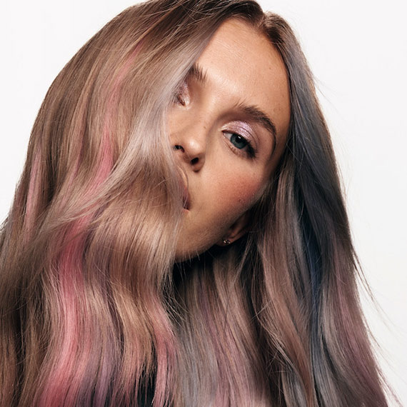 Close-up of model with ash blonde hair featuring pink and purple pastel highlights.