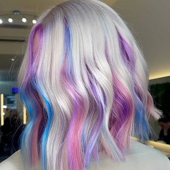 Model with silver blonde hair featuring pink, purple and blue highlights.