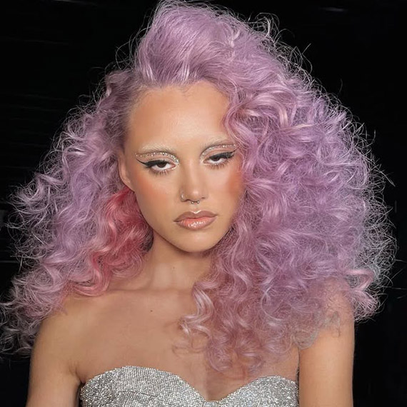 Model with full, voluminous, curly hair in shades of lilac and blush pink.