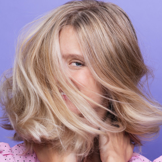 Model with long blonde hair shakes her head causing her hair to conceal her face