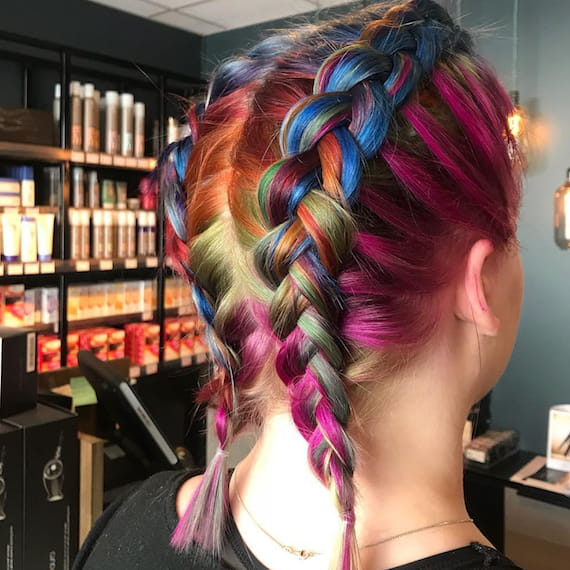 Back of a woman’s head, showing bold, jewel-toned rainbow hair plaited into a boxer braids style.