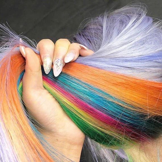 Back of a woman’s head, holding up her hair to reveal bold hidden rainbow shades underneath.